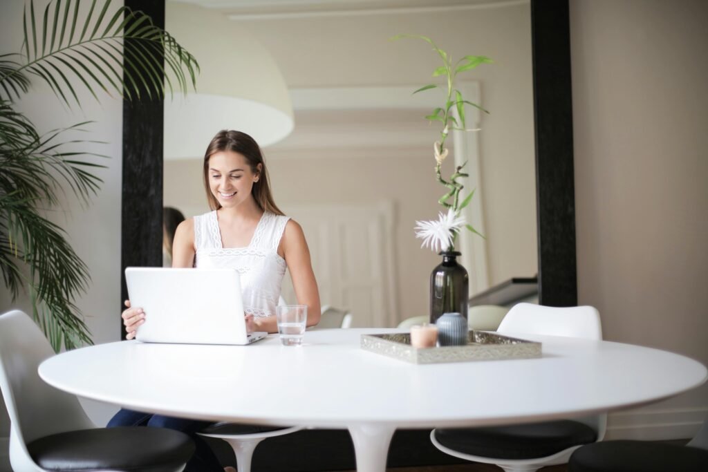 Woman in White Sleeveless Dress Sitting on Chair in Front of Table With Macbook